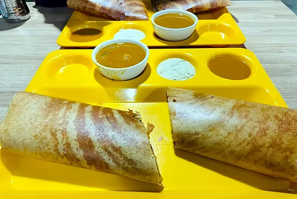 Masala dosas cut open on a yellow tray, with sambar and coconut chutney