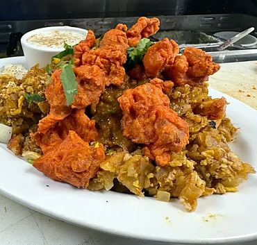 Chicken 65 biryani topped with fried chicken pieces, with raita and onion