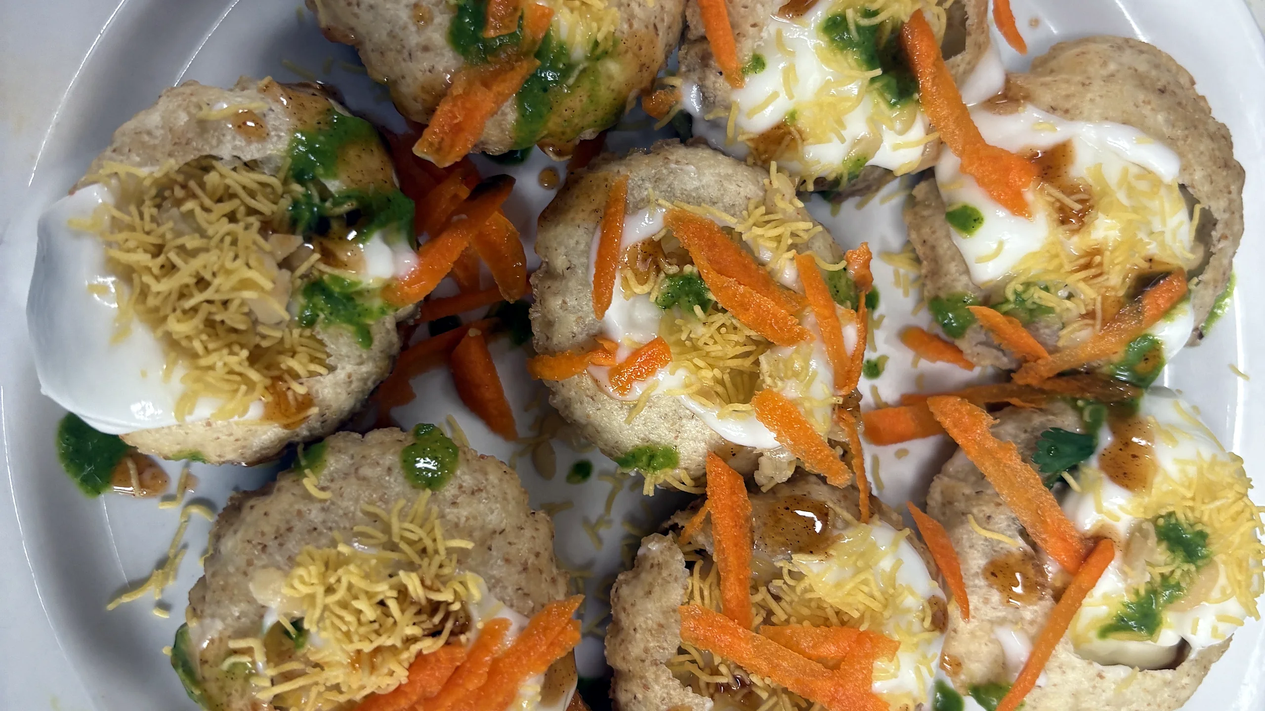 Puri chaat topped with yoghurt, sev, grated carrot and green chutney