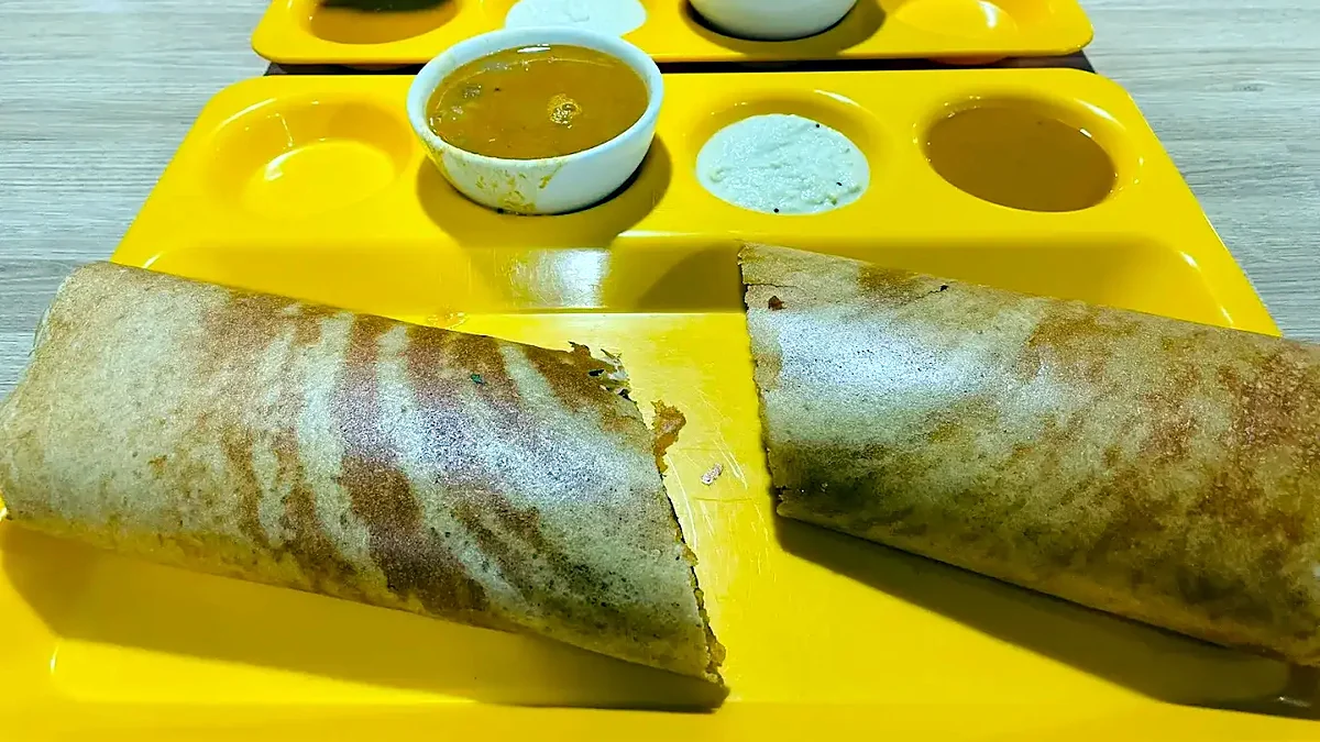 Masala dosas cut open on a yellow tray, with sambar and coconut chutney